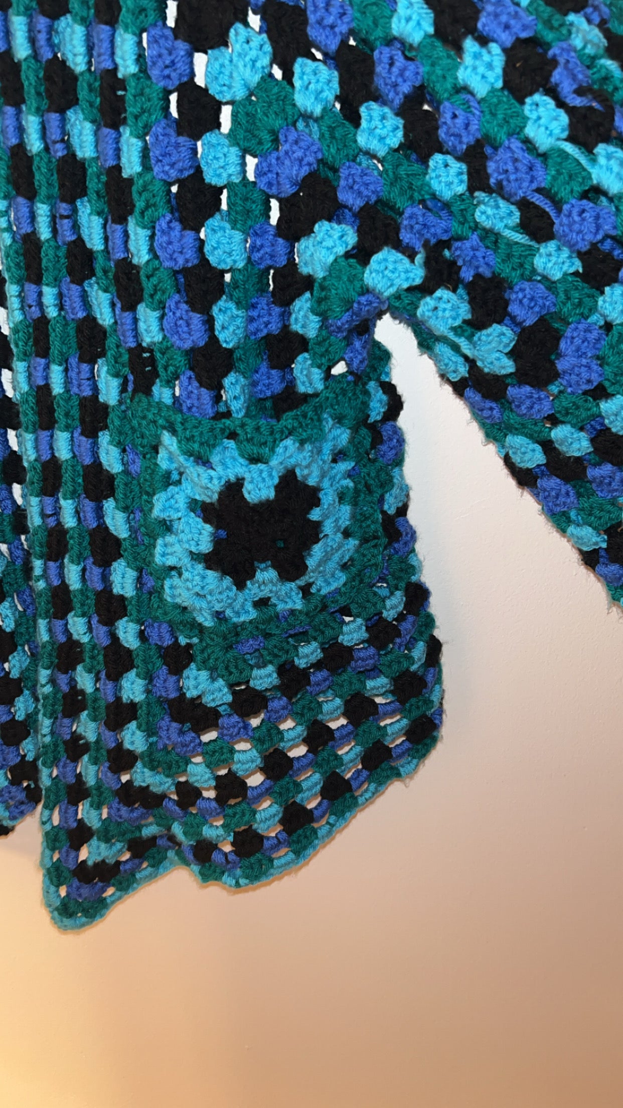 Close-up of a crocheted fabric with a grid pattern in blue, green, and black. and pocket